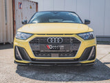 A yellow Audi car is parked on pavement, featuring a prominent hexagonal grille with Maxton design branding. Shipping containers and a white building are visible in the background.