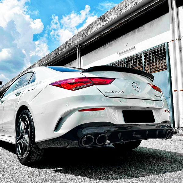 A white Mercedes-Benz CLA 250 faces away on a sunny day in an industrial area, parked near a building with a partially open garage door.