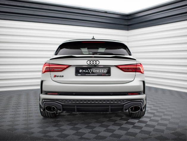 A white Audi RS Q3 sports car is stationary, viewed from the rear in a sleek, modern showroom with black and white walls. Text: "#MAXTONIZED."
