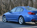 A blue sedan is parked on a paved surface, surrounded by leafless trees in a forested area.