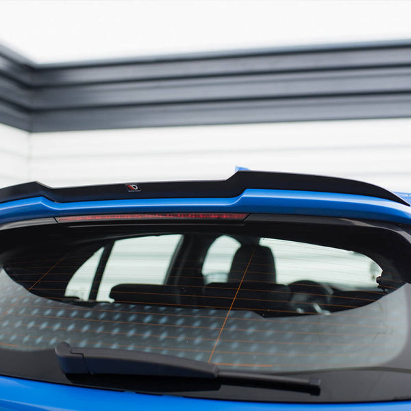 A blue car's rear window with a black spoiler is parked in a garage with horizontal wall panels. A rear wiper and an orange heating grid are visible on the window.