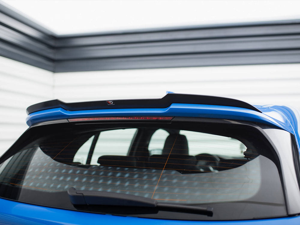 A blue car's rear window with a black spoiler is parked in a garage with horizontal wall panels. A rear wiper and an orange heating grid are visible on the window.