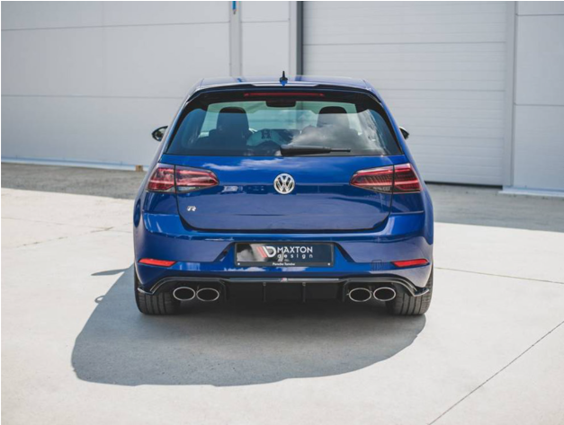 A blue Volkswagen car is parked on a concrete surface, with dual exhausts and a "Maxton Design" license plate. In the background, there's a large garage door.