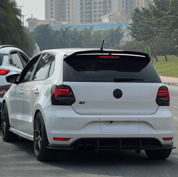 White hatchback car labeled "GT" drives on a road, flanked by another vehicle. Skyscrapers and trees form the background.