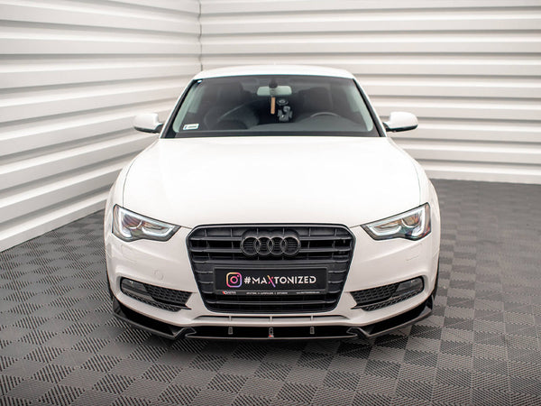 A white car faces forward in a well-lit, enclosed space with patterned flooring. Its license plate reads "INSTAGRAM #MAXTONIZED" and displays the Audi logo prominently on the grille.