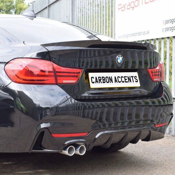A black BMW shows its rear, featuring dual exhausts and red taillights. The license plate reads "CARBON ACCENTS." It's parked by a metal fence with company signage.
