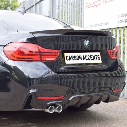 A black BMW shows its rear, featuring dual exhausts and red taillights. The license plate reads "CARBON ACCENTS." It's parked by a metal fence with company signage.