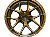 A bronze alloy car wheel rim with a multi-spoke design is displayed against a plain white background. The rim features a central hub and five bolt holes.