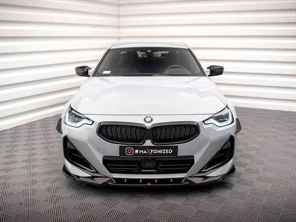 A white BMW car is stationary in a minimalist room with geometric walls and flooring. The front grille and headlights are prominent. Text on the car reads "#MAXTONIZED."