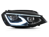 A car headlight is illuminated, showcasing its LED design with a sleek, angular shape. It is set against a plain white background, emphasizing its modern aesthetic.