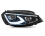 A car headlight is illuminated, showcasing its LED design with a sleek, angular shape. It is set against a plain white background, emphasizing its modern aesthetic.