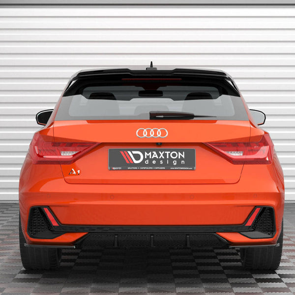 An orange Audi A1, parked on a checkered floor, faces a white garage door. The rear displays the logo and "Maxton Design" on the license plate area.