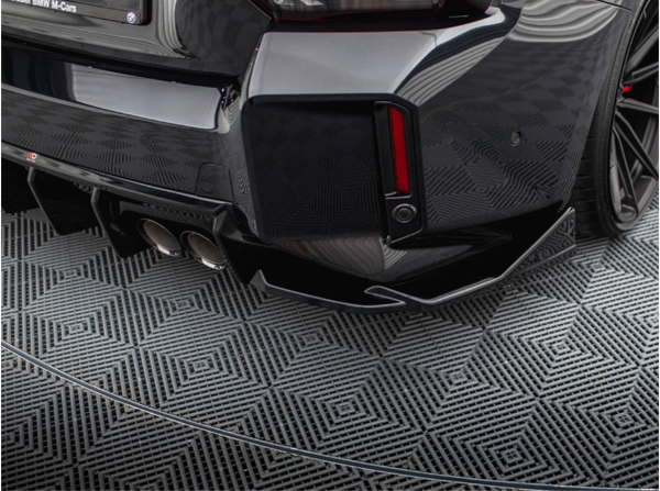 A car's rear bumper displays dual exhaust pipes and a sleek design, resting on a patterned, geometric floor. The surroundings are minimal, highlighting the vehicle's modern aesthetic.