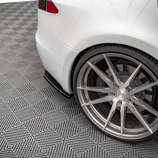 A white car is parked, showcasing its sleek, large alloy wheel on a patterned grey floor, emphasizing the vehicle's sporty design and modern environment.