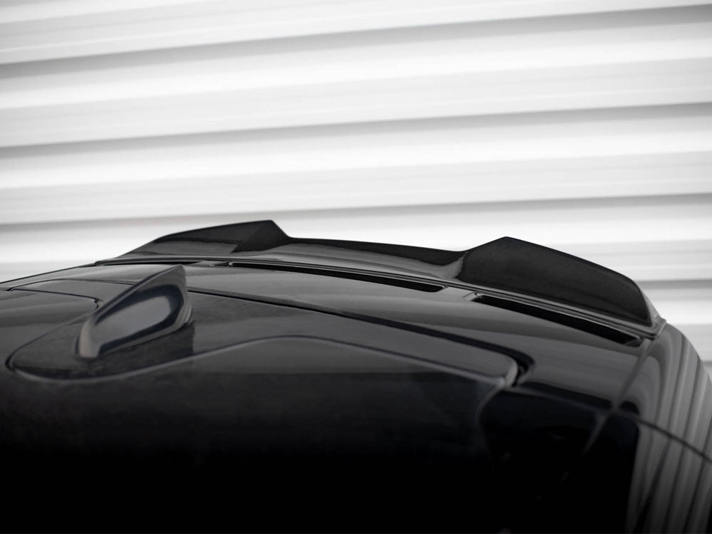 A black car roof features a shark fin antenna and two sleek air inlets. The background displays horizontal white ridges, resembling a garage door or wall paneling.