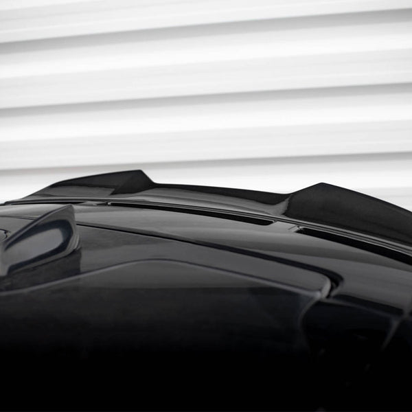 A black car roof features a shark fin antenna and two sleek air inlets. The background displays horizontal white ridges, resembling a garage door or wall paneling.