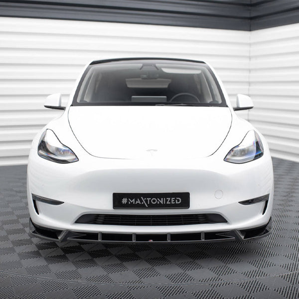 A white car is parked in a futuristic showroom with striped walls and a checkered floor. The license plate displays "#MAXTONIZED."