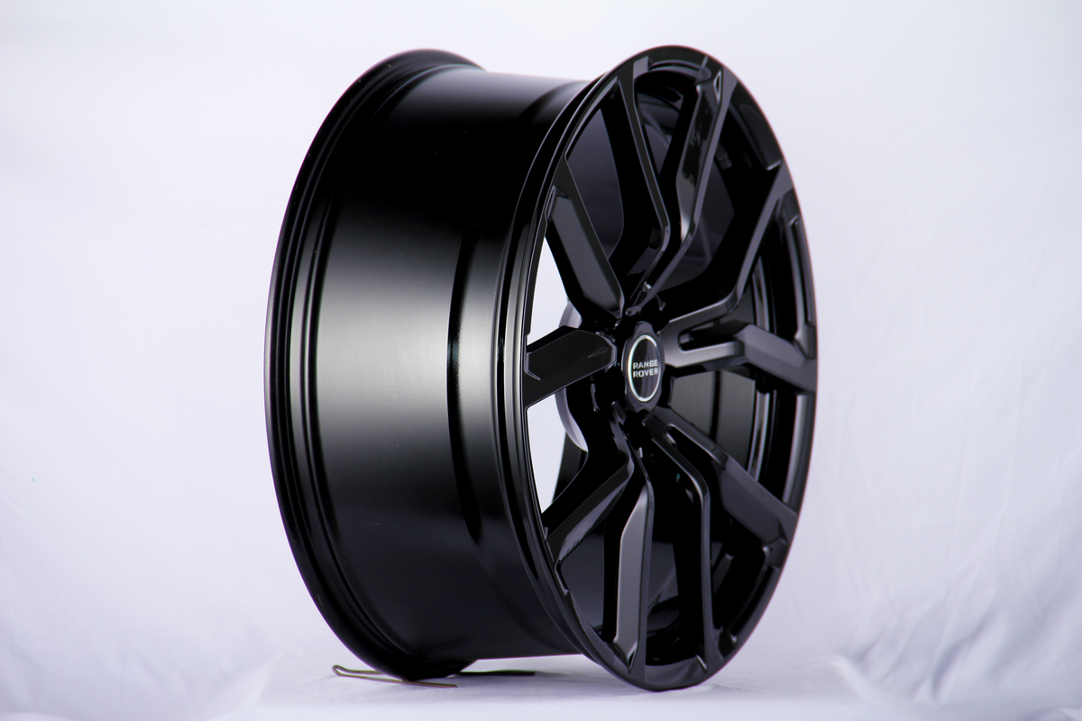 A shiny black alloy wheel, with "RANGE ROVER" text on the center cap, stands upright against a plain white backdrop.