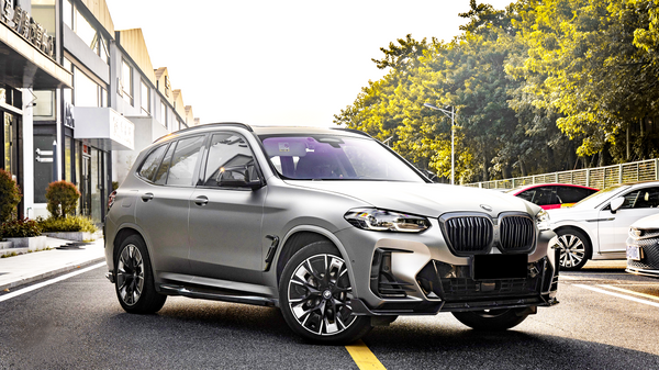 A gray SUV is parked on a sunlit street, surrounded by buildings and trees. Other cars are parked nearby.