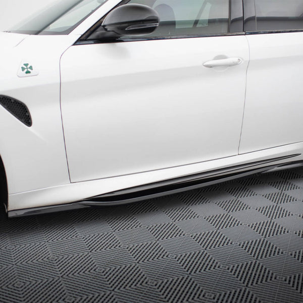 A white car is parked, showcasing its side view with a clover emblem near the front fender. It rests on a textured, patterned flooring.