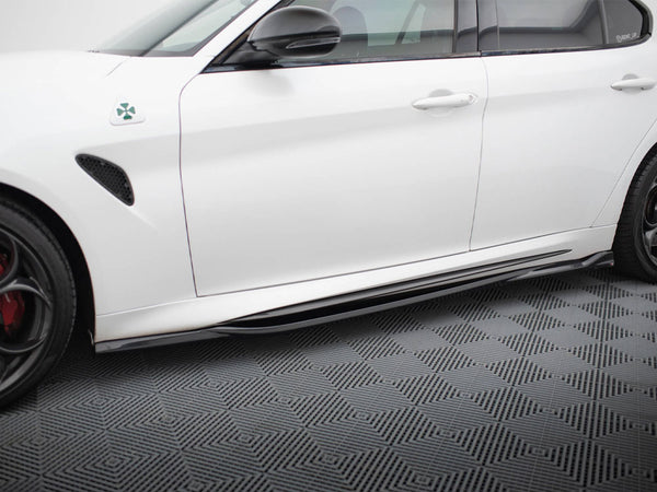A white car is parked, showcasing its side view with a clover emblem near the front fender. It rests on a textured, patterned flooring.
