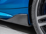 A blue car with a carbon fiber side skirt is parked, featuring a detailed close-up of its wheel and tire on a smooth concrete surface.