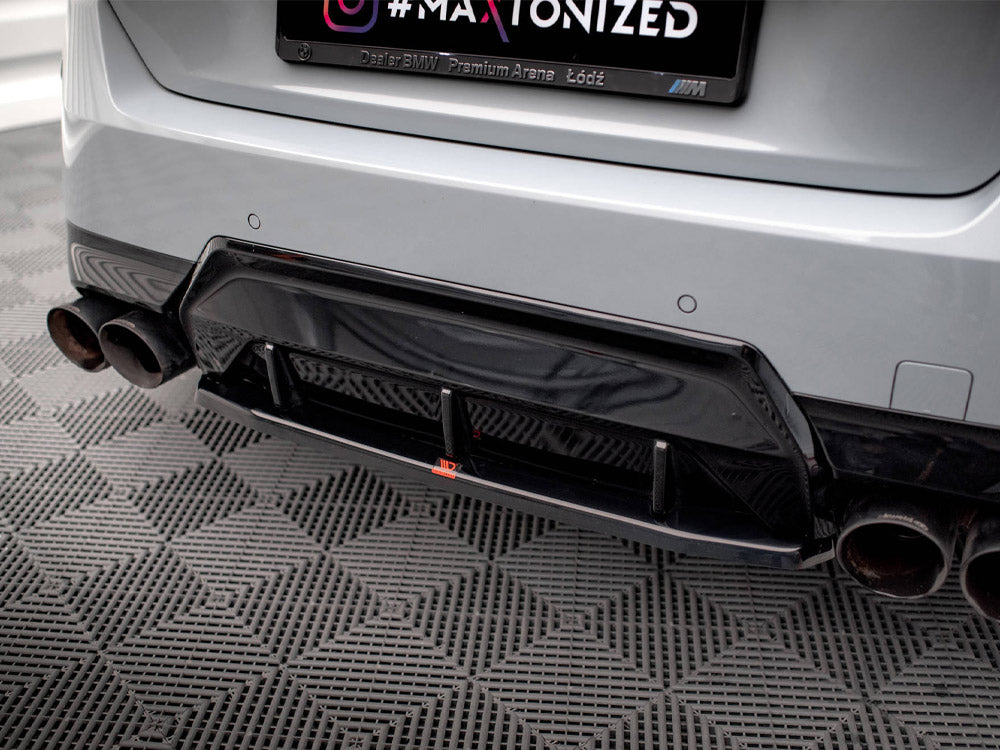 A car's rear bumper features a black diffuser and dual exhaust pipes on a patterned floor. The license plate frame reads “Dealer BMW Premium Arena Łódź.”