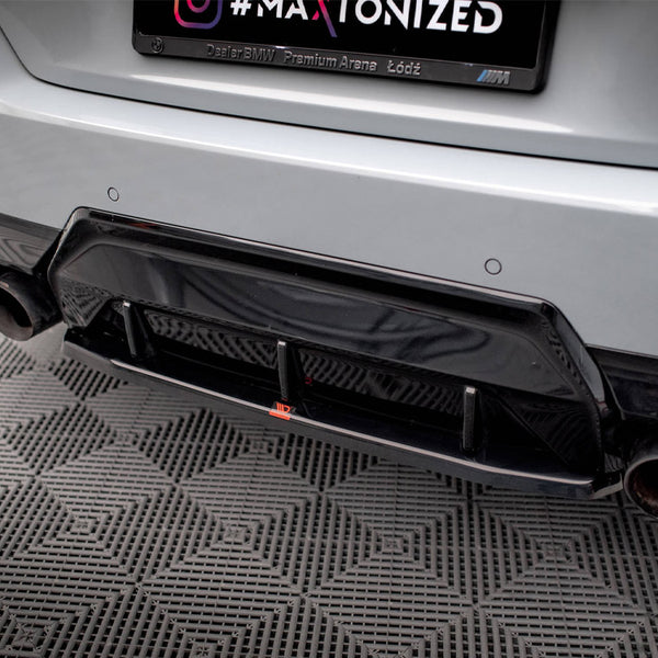 A car's rear bumper features a black diffuser and dual exhaust pipes on a patterned floor. The license plate frame reads “Dealer BMW Premium Arena Łódź.”