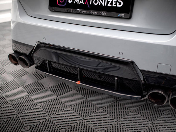 A car's rear bumper features a black diffuser and dual exhaust pipes on a patterned floor. The license plate frame reads “Dealer BMW Premium Arena Łódź.”