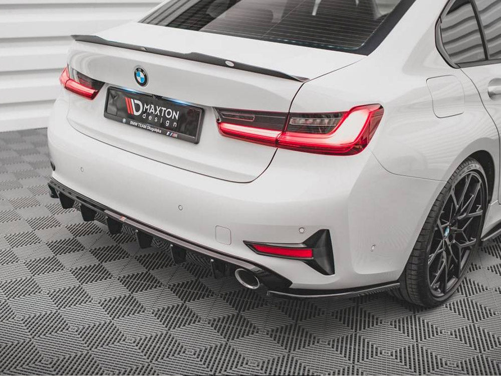 A white car with a BMW badge stands parked, featuring a rear spoiler. The license plate displays "DMAXTON design, BMW TEAM Dloposka." It rests on a gray geometric-patterned floor.