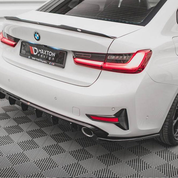 A white car with a BMW badge stands parked, featuring a rear spoiler. The license plate displays "DMAXTON design, BMW TEAM Dloposka." It rests on a gray geometric-patterned floor.