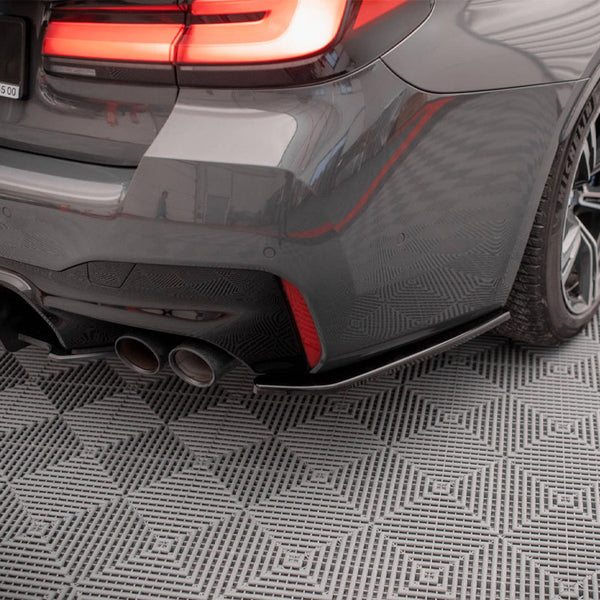 The rear of a grey car features illuminated taillights and dual exhaust pipes, stationary on a patterned floor. Visible text: "MAXTON design, J. Conrada 20, (12) 211 45 00."