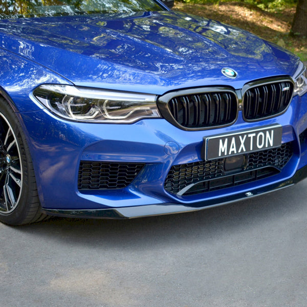 A blue car with a black grille and "MAXTON" license plate is parked on a paved road, surrounded by trees.