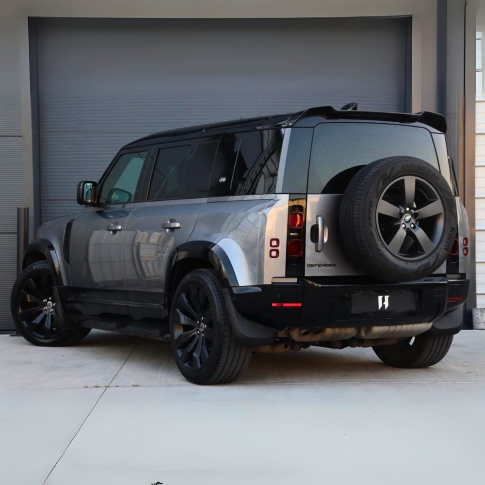 A gray SUV with a spare tire on the back is parked in front of a large, closed garage door. The vehicle is branded "Defender."