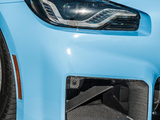 A car's blue front end features an angular headlight and a carbon fiber air intake, with a smooth surface and tire visible, suggesting a sleek, sporty design parked on asphalt.