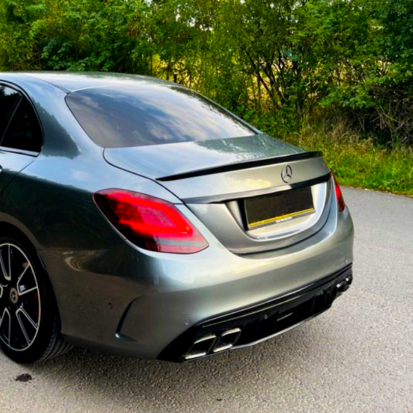 A gray sedan is parked on a quiet road, surrounded by lush green trees and bushes.