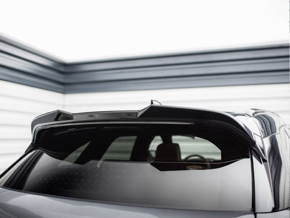 A car features a glossy black rear section with a spoiler. It's parked in a brightly lit garage with striped metal walls in the background.