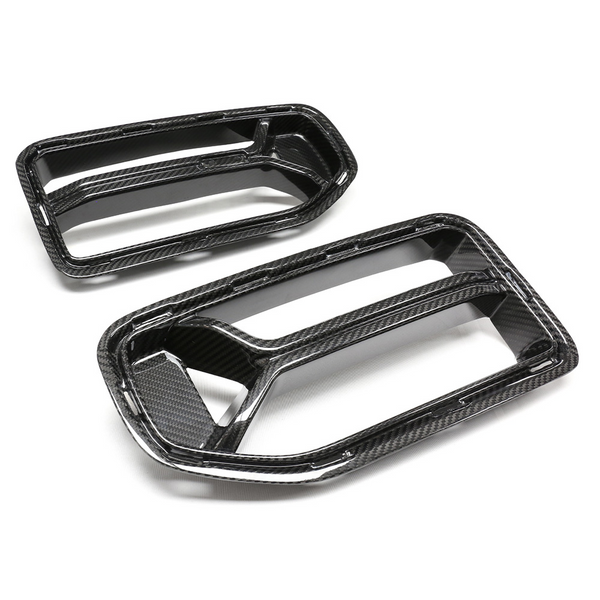 Two carbon fiber air intake covers with rectangular openings lie on a flat, white surface. The glossy finish highlights their texture, designed for automotive use, suggesting a performance-focused application.