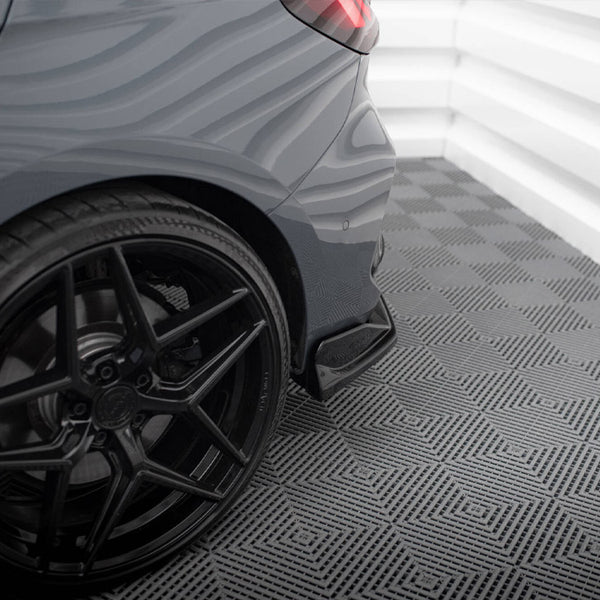A car's rear tire and wheel resting on a patterned floor, in a brightly lit, white-walled indoor space. The environment is clean and modern, emphasizing the car's sleek design.