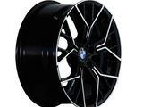 A black alloy wheel with intricate silver accents rests upright, featuring the blue and white circular BMW logo at its center, isolated against a plain white background.