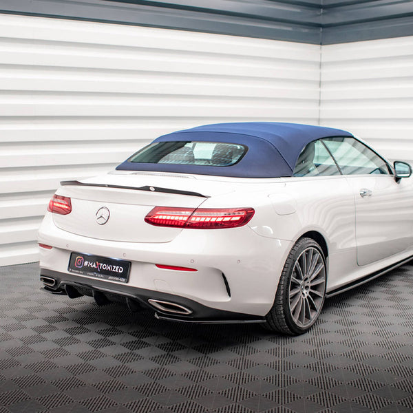 A white convertible car with a blue soft top is parked in a modern showroom with patterned flooring and white paneled walls. Visible text: "MATIONIZED" on the license plate.