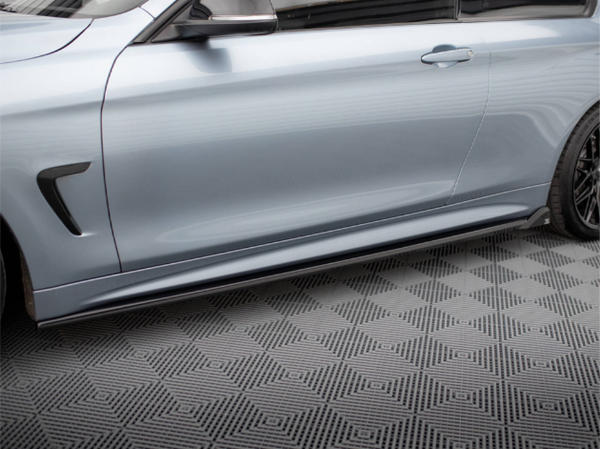 A metallic silver car with sleek side skirts is parked on a geometric-patterned floor, emphasizing its modern design and low profile. The car's door and wheel are partially visible.