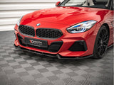 A red sports car with sleek design and illuminated headlights is stationary on a textured gray floor. The front grille displays a badge, and 