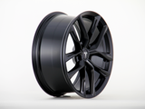 A black alloy wheel with a sleek, multi-spoke design displays a central logo resembling a 