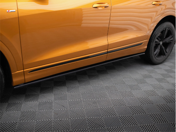 An orange car door remains static, with its sleek design reflected in an orange exterior. The vehicle is parked on a textured, patterned grey surface indoors.