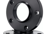 A black metal flange with six bolt holes stands upright, placed atop a similar base flange, in a plain white background.
