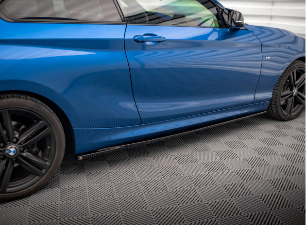 A blue car is parked, partially visible, showing its side profile with black wheels in a room with a patterned floor and a white, lined wall.