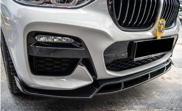 Car front bumper with a sleek design, featuring a detailed grille and a decorative emblem. The vehicle is parked on a metal-patterned surface, suggesting an outdoor or garage setting.