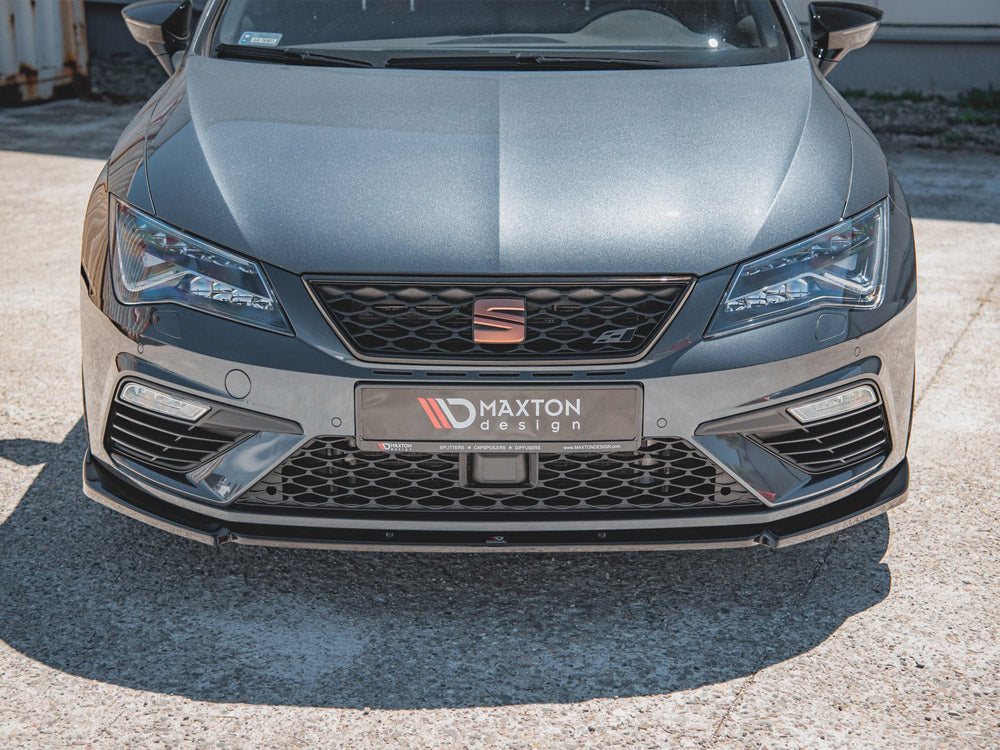 A sleek grey car displays a Maxton Design front bumper with sharp headlights in a sunlit parking area. The front plate reads, “MAXTON design” and includes small text: “SPLITTERS COMPOSITES DIFFUSERS www.MAXTONDESIGN.com.”