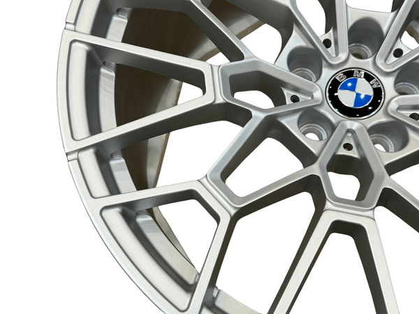 A silver alloy wheel displaying a multi-spoke design with a central BMW logo, photographed against a plain background, highlighting its detailed structure and sleek metallic finish.